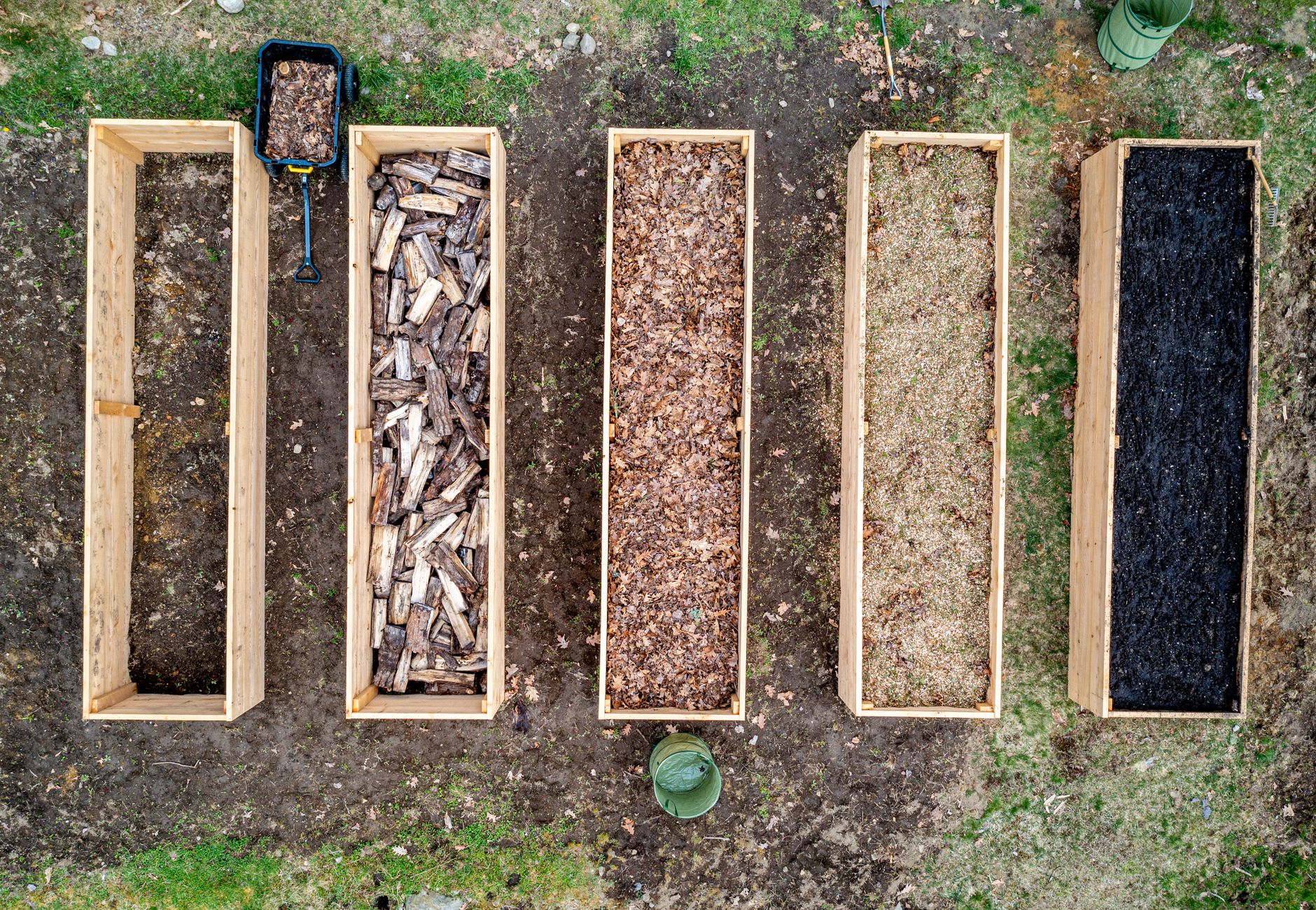 Top view of wooden boxes with piles of firewood wood chips sawdust and coal placed on ground in agricultural plantation