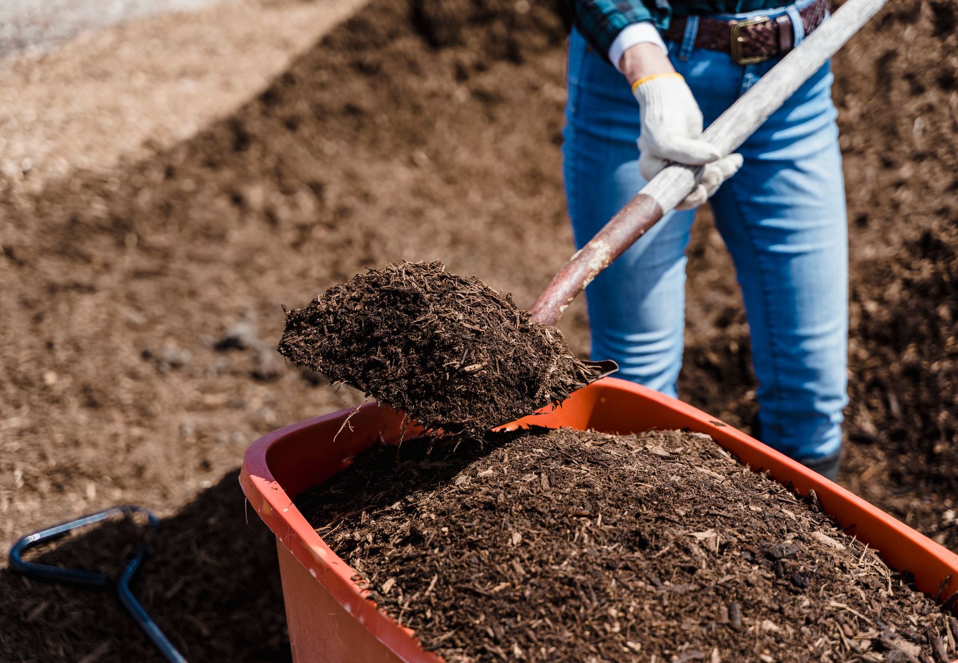 A person shovels compost into a red container, preparing soil for gardening.