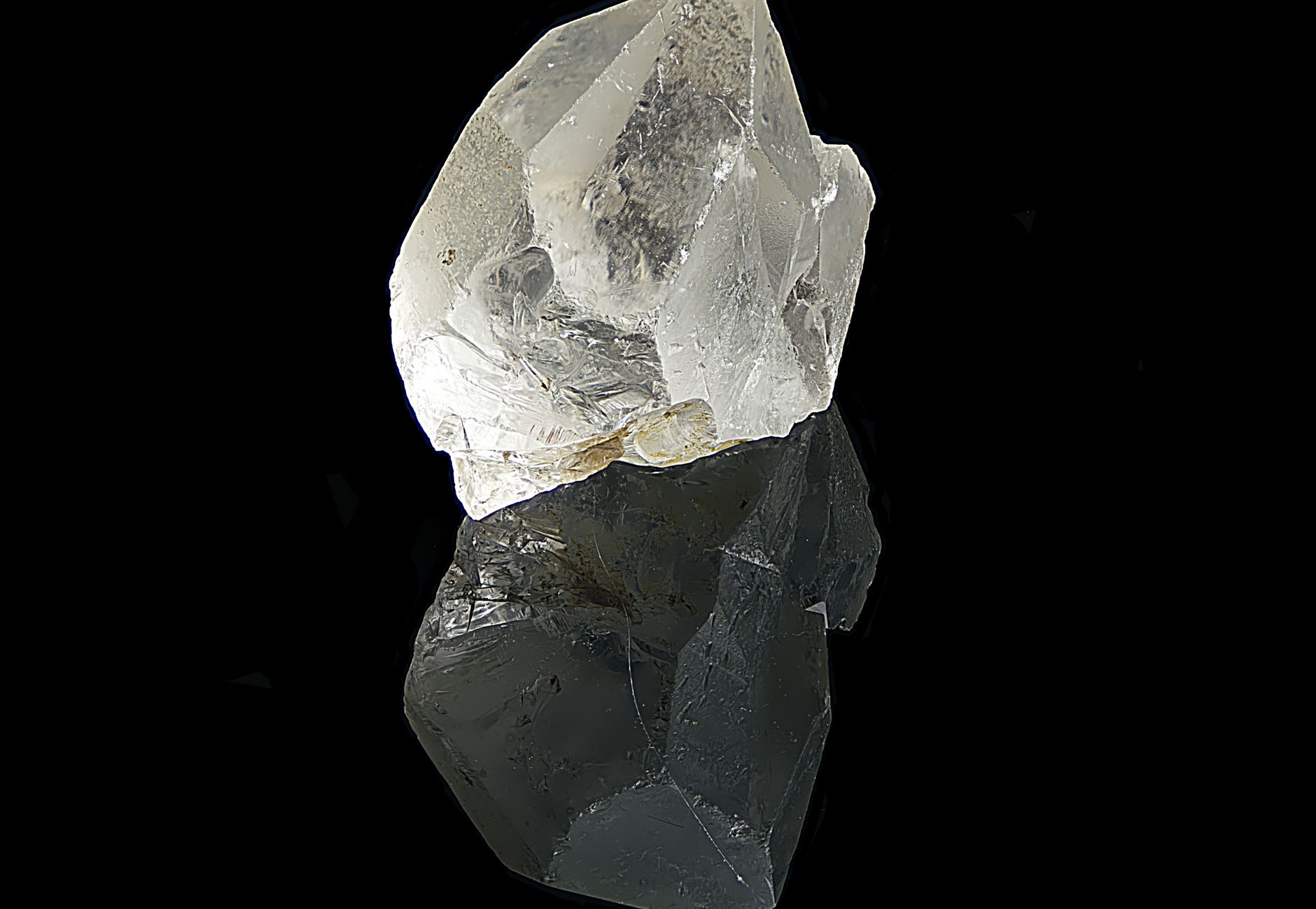 Clear quartz crystal with reflection against black background, showcasing natural beauty.